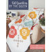 The front cover of the Fat Quarters By The Dozen book featuring a colorful quilt draped over a chair, featuring floral patterns in red, orange, and blue.