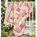 The completed Easy as ABC and 123 quilt kit colored in soft red, pink and white fabric from the  Yours Truly collection by P&B Textiles, draped over a white porch surrounded by pink roses.