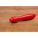A close up on the Un-Stitcher, a red handheld tool with a pointed metal tip, resting on a wooden surface.