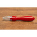 A close up on the Un-Stitcher, a red handheld tool with a pointed metal tip, resting on a wooden surface with the cap on.