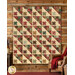 The completed Hodgepodge Quilt colored in warm brown, tan, cottage blue, and berry red fabrics from the Always and Forever collection by Andover Fabrics, hung on a log cabin wall and staged with coordinating furniture and décor.