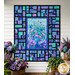 The completed Stained Glass Panel Quilt, colored in blue, teal, and purple fabrics from the Bellagio collection by Timeless Treasures Fabrics, hung on a white paneled wall and staged with potted plants.