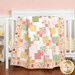 Image of the completed Disappearing 9-Patch Crib Quilt - Baby Girl in pink, green, and yellow fabrics, draped over the side of a white crib, with coordinating nursery décor.