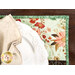 A stylized close up on the top corner one of the placemats, showing details on the fabric colors, prints, and top quilting; a coordinating table setting sits atop.