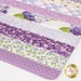A patchwork fabric featuring various purple floral and patterned strips with a polka dot border.