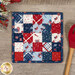 The completed Fusible Grid Hot Pad colored in red, blue, and white fabrics from the Stars & Stripes Forever collection by Riley Blake Designs. The project is staged on a wood table where a wooden spoon and patriotic garland peek into frame.