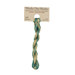 A skein of variegated light green and flax embroidery floss, twisted and bundled, with a tan label featuring the brand name and color information.