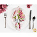 A shot of one of the napkins with the floral print faced out, staged on a white plate with a brushed nickel napkin ring.