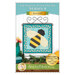 Front cover of the August pattern featuring the completed Foundation Paper Piecing Series 4 August project, a teal and yellow design of a bumblebee, displayed on a craft stand and staged with coordinating décor.