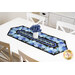 The completed Easy Striped Table Runner colored in bold blue floral print fabrics from the Escapade collection, staged on a clean white table with a vase containing blue flowers.