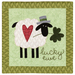 The completed On Wander Lane Mini Quilt for March, with an appliqué sheep with a hat on its head and a heart on its fleece, holding a shamrock in its mouth, beside hand-stitched text that reads "lucky ewe." The project is isolated on a white background.