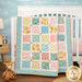 The completed Charming Windows Quilt colored in pastel primary colors from the Rainbow Dreams collection by Wilmington Prints, draped over a white crib in a nursey with coordinating décor.