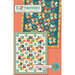 Front of the Extrovert pattern showing digital images of two versions of the completed quilt in summery gold, navy, cream, and turquoise tones featuring geometric designs, on an orange background with the title of the pattern in a banner across the top.