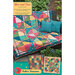 Front of the Slice and Dice pattern showing the completed quilt, featuring bright colored geometric blocks, draped over a wicker couch with teal pillows. The title of the pattern featured in a gold banner across the top.