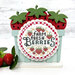 The fully assembled and painted Strawberry Basket Cross Stitch Display with a finished cross stitch project mounted on it that says "Farm Fresh Berries", staged on a white tabletop with strawberries.