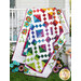 The completed Ambrosia quilt colored in vibrant fabrics from the Sunburst Batiks collection by Moda Fabrics, artfully draped over a white porch railing and staged with coordinating flowers and garden décor.