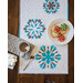 A quilted table runner displays snowflake patterns, with a plate of decorated cookies and a cup of hot chocolate.