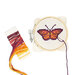 A cross-stitch hoop featuring a butterfly design, with colorful embroidery threads beside it.