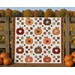 Digital mockup of the Cozy Autumn quilt featuring patchwork pumpkins, falling leaves, and hearts, set in a pumpkin patch, hanging on a fence