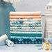 A stack of the fabrics included in the Gulf Breeze collection, with a jar and flowers and a seashell and a starfish and a ceramic lighthouse and thread.