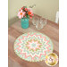 A round table topper with a bursting star design in light pink, mint, teal, and cream fabrics placed on wooden table next to three glasses and a bouquet of flowers. 