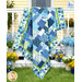 The completed Easy as ABC Quilt Kit in green, light blue, blue, and white fabrics from the Blueprint collection by Moda, hung over a white railing surrounded by yellow and blue flowers. 