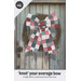 A colorful patchwork bow with wide tails adorns a rustic wreath on a weathered door.
