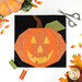 A top down shot of the unfinished October block, a jack-o'-lantern in orange, yellow, green, and black fabrics, laid flat on a white tabletop with coordinating décor and sewing supplies. 