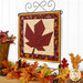 The completed Foundation Paper Piecing Series 4 November project, featuring a maple leaf in warm rust red, mahogany, and cream prints, displayed on a craft hanger and staged with coordinating foliage.