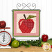 The completed Foundation Paper Piecing Series 4 September project, an apple in red, cream, and green fabrics, staged on a craft hanger on a wooden table with coordinating décor.