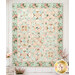 The completed Rose Hill Lane Quilt, colored in gentle mint, blue, cream, and pink vintage fabrics from the Rose & Violet's Bouquet des Fleurs collection by Riley Blake Desings, hung on a white wood wall and staged with coordinating flowers.