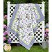 The completed Patchwork Quilt colored in periwinkle, lilac, green, and white fabrics from the Hydrangeas In The Garden collection from Riley Blake Designs, artfully draped over a white lattice and surrounded by lush hydrangeas.
