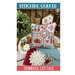 A white, red, and blue decorative pillow featuring intricate patterns, surrounded by sewing items and greenery.