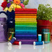 A stack of vibrant, multicolored fabric rolls arranged in rainbow order, surrounded by jars and flowers.