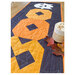 A stylized shot of the Ghostly Greetings table runner on a wooden table, fall décor sit in the foreground. 