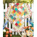 The finished Charming Picnic Quilt Kit completed in red, teal, orange and grey fabrics from the In The Garden collection, artfully draped over a white fence with coordinating flowers.  