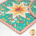 A close up on the square hot pad, demonstrating color and print details on the teal, vermillion, and orange fabrics.