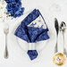 A top down shot of the napkin with the dark blue side out; the napkin is staged with a white plate, silverware, and matching cup.