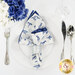 A top down shot of the napkin with the white side out; the napkin is staged with a white plate, silverware, and matching cup.