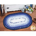 The completed Jelly Roll Rug colored in dark blue, blue, and white fabrics from the Blue Belle collection by Maywood Studio, staged beside a white dresser. 