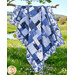 The completed Easy as ABC Quilt Kit in dark blue, blue, and white fabrics from the Blue Belle collection by Maywood Studio, hung over a tree branch surrounded by a scenic field of flowers. 