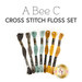 A set of seven cross stitch floss threads in brown, teal, yellow, and gold colors below a text graphic..