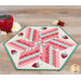 The completed 60 Degree Diamond Table Topper colored in bright pink, red, and green fabrics from the Berry & Sage collection by Riley Blake Designs, staged on a rustic wood table and paired with coordinating strawberries and daisies.