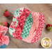 A top down shot of one of the bowl cozies in red, pink, and green fabrics, staged on a wood table with strawberry pincushions.