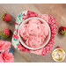 A top down shot of one of the bowl cozies in red, pink, and green fabrics, holding a white bowl of strawberry ice cream, staged on a wood table with strawberry pincushions.