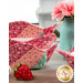 A close up on the stack of bowl cozies, colored in red, pink, and green fabrics, staged on a wooden table with coordinating décor and strawberry pincushions. 