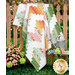 The completed Ridiculously Easy Jelly Roll Quilt colored in bright fabrics from the Summer Skies and Fireflies collection by Riley Blake Designs, artfully draped over a brown picket fence with coordinating flowers.