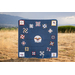 Blue quilt displayed outdoors in a field with mountains in the background.