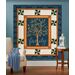 The completed Family Tree Patchwork Panel Quilt, colored in blue, cream, and brown fabrics from the Family Tree collection by Moda Fabrics, staged on a blue wall with coordinating décor.