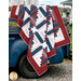 The completed Steadfast Quilt finished in patriotic themed fabrics from the American Gatherings III collection by Moda fabrics, draped over the side of a old blue truck. 